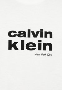 Czarny, pogrubiony tekst "calvin klein" z mniejszym napisem "New York City" poniżej na białym tle z tkaniny.