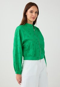 Groene bomberjack met een ritssluiting aan de voorkant, bloemen snijmotief en elastische manchetten. Gemaakt van lichtgewicht stof en heeft een ontspannen pasvorm.