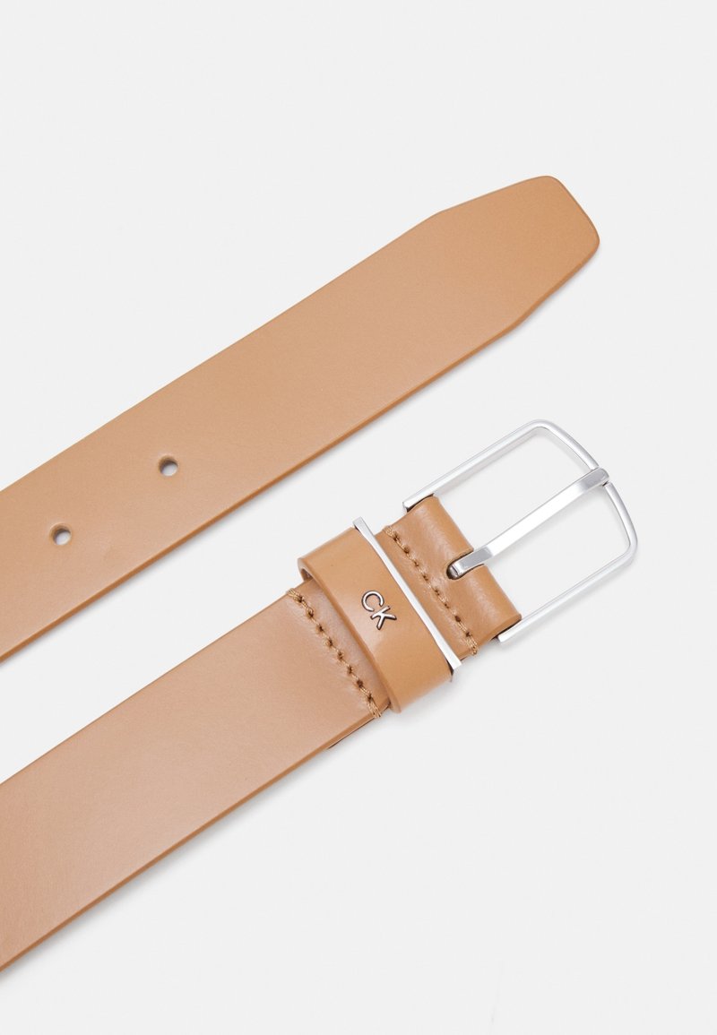 Ceinture en cuir brun clair avec boucle rectangulaire argentée et logo "ck" sur la boucle de ceinture sur fond blanc uni.