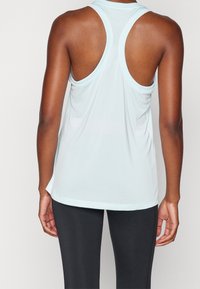 Vaaleansininen urheilullinen tanktoppi, jossa on kilpa-ajan malli, sileä pinta ja hieman kaareva helma. Yhdistetty tummiin leggings-housuihin.