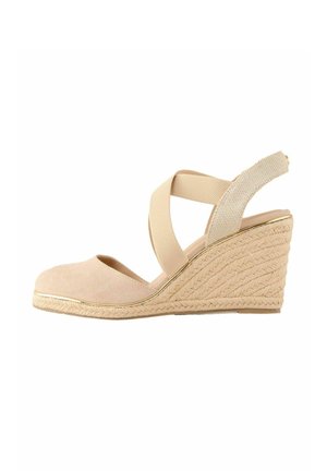 Beige suede wedge shoe with crisscross elastic straps and textured jute sole. Features a smooth rounded toe and gold accent along the sole.