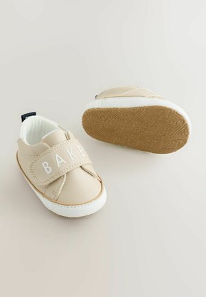 Beżowe dziecięce trampki z wierzchem przypominającym skórę, elastycznym paskiem z napisem "BAKED", białymi akcentami oraz teksturowaną gumową podeszwą.