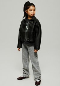 Must musta läikiv nahkjope graafilise t-särgi peal, koos heledate hallide teksadega, millel on valged kaunistused, ja tumejalatsitega.