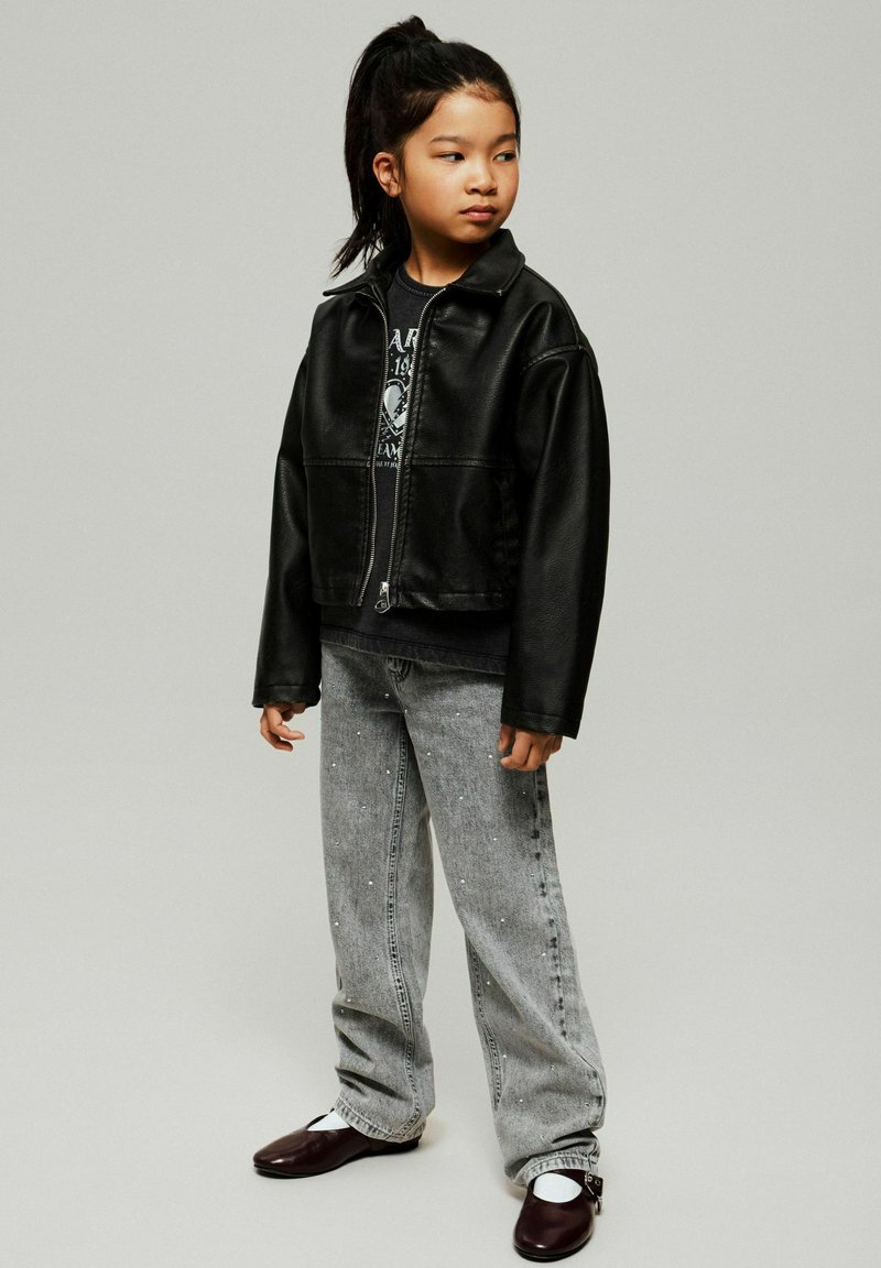 Must musta läikiv nahkjope graafilise t-särgi peal, koos heledate hallide teksadega, millel on valged kaunistused, ja tumejalatsitega.