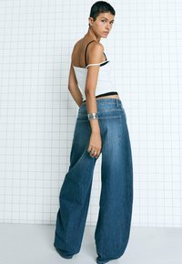 Vida jeans i lång modell i blå denim med hög midja, kompletterad med en åtsittande vit linne. Har en slät yta och en minimalistisk design.