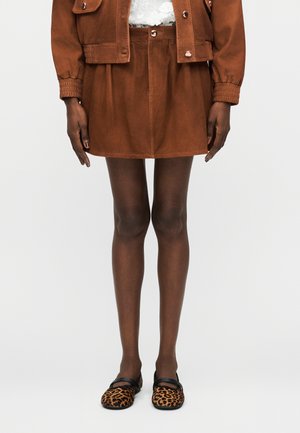 Hnedá semišová sukňa a zodpovedajúca bunda nosené s čiernymi pančuchami a leopardími plochými topánkami s čiernymi remienkami.