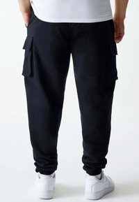 Zwarte cargobroek met zijzakken, elastische cuffs en een relaxte pasvorm, gecombineerd met witte sneakers. Zachte stof met een gladde textuur.