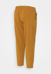 Hořčicové kalhoty s pružným pasem, zúženými nohavicemi, bočními kapsami a hladkým, pružným materiálem.