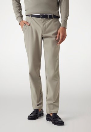 Beige Hosen aus glattem Stoff, mit normaler Passform und vorne Taschen, kombiniert mit schwarzen Mokassins.