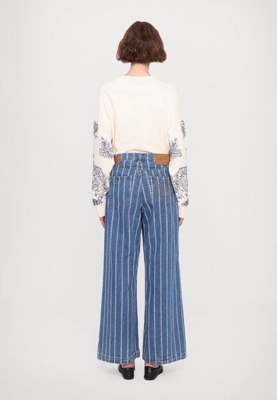 Wide-leg blue striped jeans with a high waist, paired with a cream sweater featuring blue floral patterns on the sleeves. Black shoes visible.