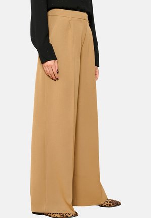 Pantaloni a gamba larga color cammello con pince, realizzati in tessuto morbido. Abbinati a un top nero a maniche lunghe e scarpe con stampa leopardata.