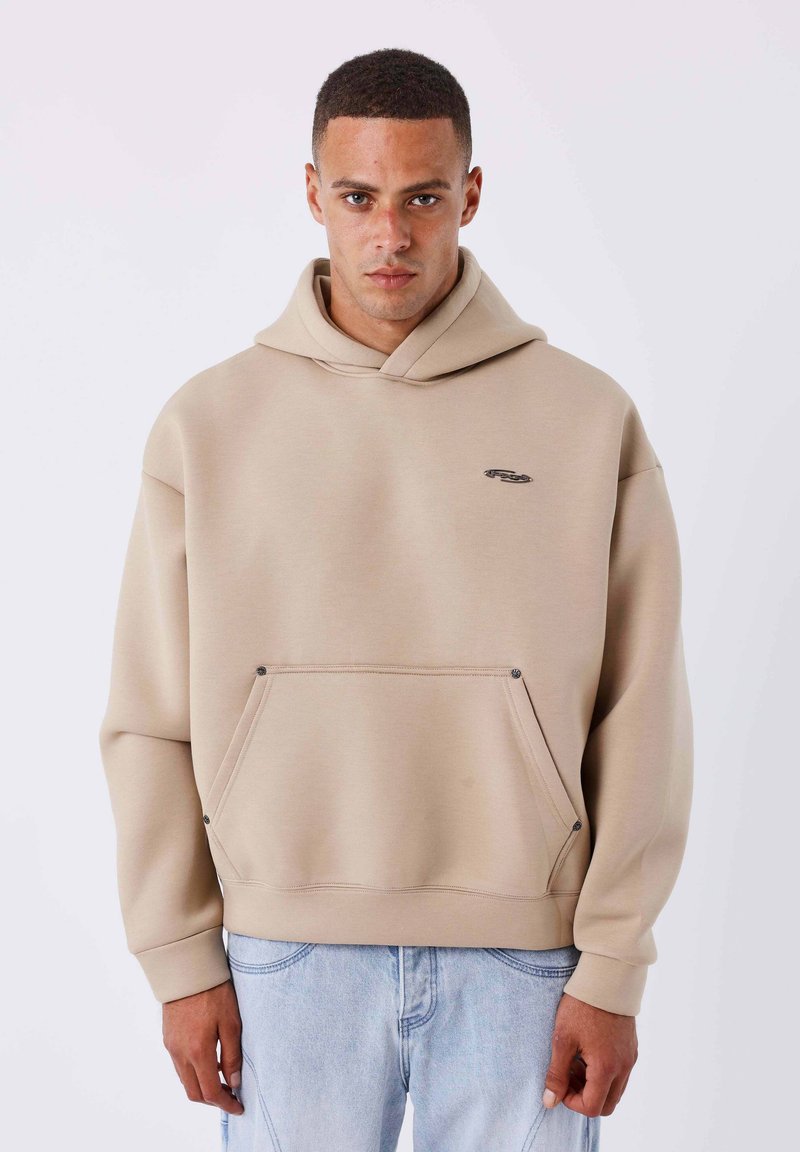 Sudadera con capucha beige hecha de tela suave, que presenta un gran bolsillo frontal, detalles mínimos de costuras y un pequeño logo en el pecho.