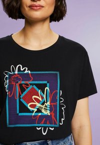 Sort t-shirt med farverige geometriske blomstergraphics i rød, gul og blå, med rund halsudskæring og korte ærmer.