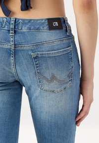 Vaqueros de denim azul con un diseño ajustado, con una etiqueta negra de LTB en la cintura y un patrón de costura destacado en el bolsillo trasero.