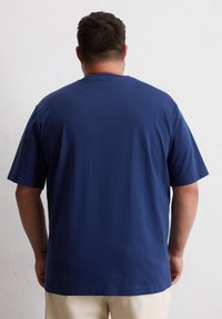 T-shirt bleu marine à manches courtes en coton. Il présente un col rond et une coupe décontractée, avec une texture lisse et des détails de conception minimalistes.