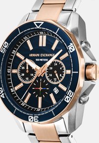 Roostevaba terasest ja roosa kuld karp, millel on tumesinine kelladial, kolm aldiali, lumineeruvad tunniindikaatorid ja veekindlus kuni 100 meetrit.