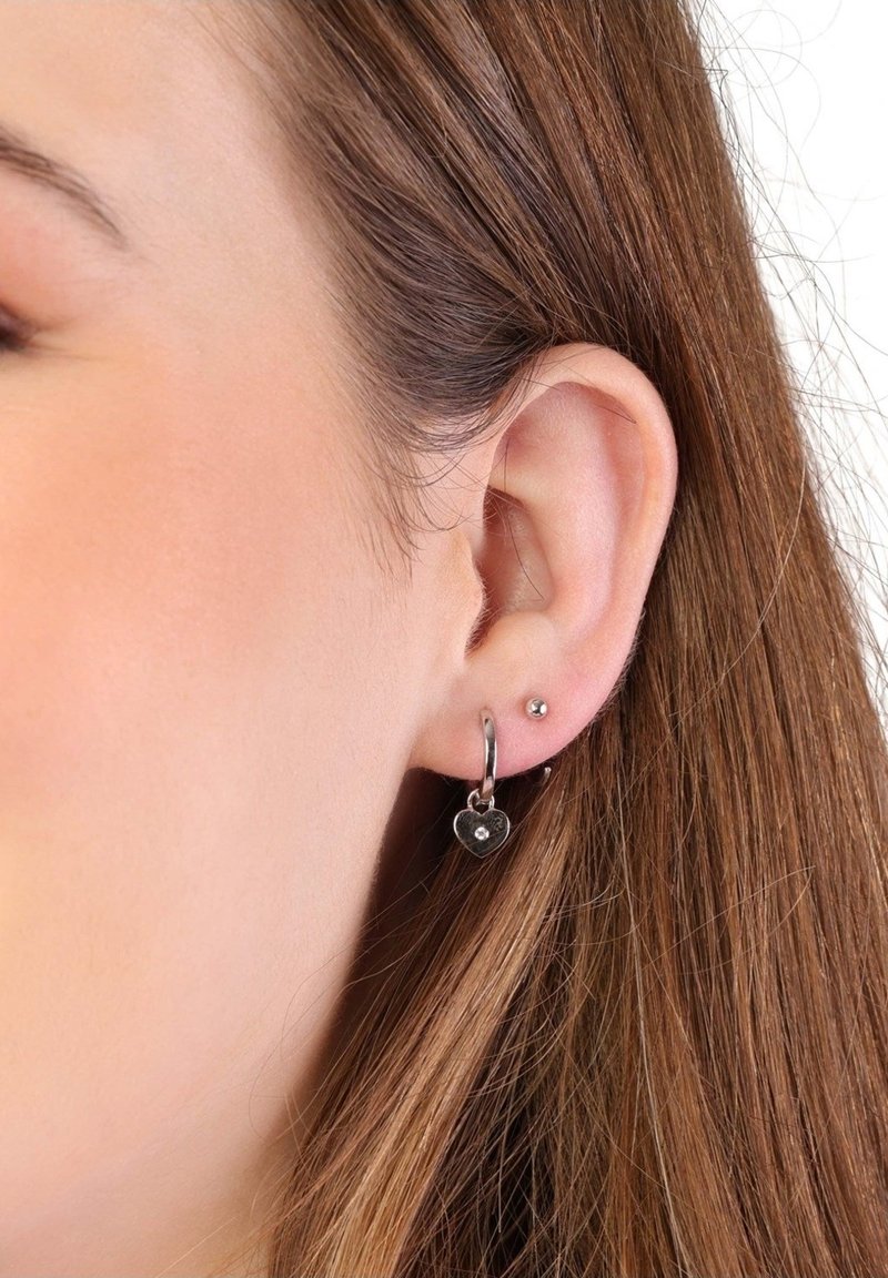 Boucles d'oreilles créoles en argent avec un charme en forme de cœur orné d'une petite pierre précieuse. Accompagnées d'une simple boucle d'oreille en argent. Texture lisse.