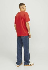 Rød kortærmet T-shirt lavet af bomuld, parret med loose blå denimbukser og beige sneakers med grønne accenter.