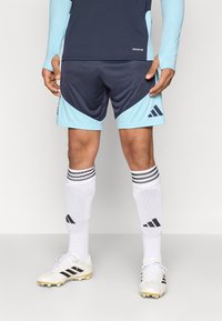 Αθλητική στολή Adidas με ναυτικά σορτς με ανοιχτό μπλε λεπτομέρειες, λευκές κάλτσες με μαύρες ρίγες και λευκά παπούτσια με μαύρες λεπτομέρειες.