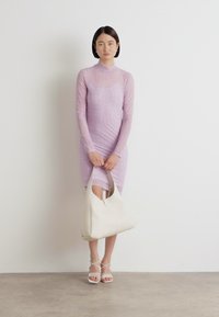 Light purple, long-sleeve dress with ribbed texture and bodycon fit. Model holds a white leather handbag and wears strappy white sandals.