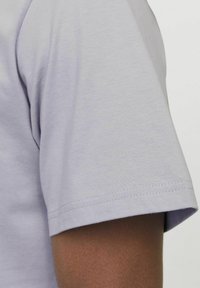 Lyse lilla bomulds t-shirt med rund halsudskæring og korte ærmer, der viser en glat tekstur og rene syninger på ærmet.