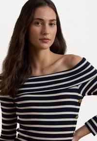 Navy og kremstripe av skuldrene topp med ribbet tekstur og gullfarge knapper på venstre side.