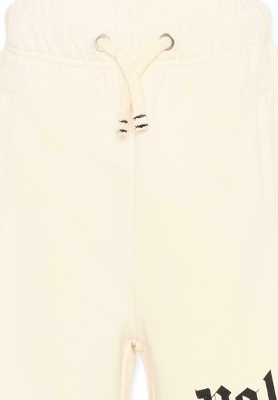 Pantalon de survêtement blanc cassé avec taille à cordon de serrage et texte noir partiellement visible près du bas.