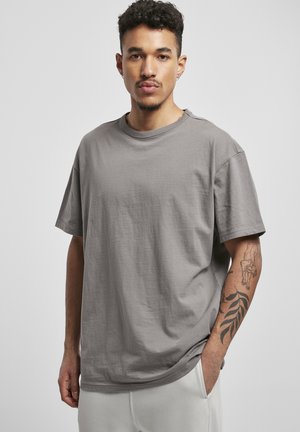Tricou din bumbac gri cu o croială lejeră, guler rotund, mâneci scurte și textură fină. Prezintă cusături vizibile și o fente pe lateral.
