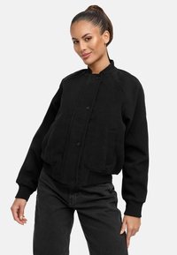 Black bomber jacket made of textured fabric, featuring a ribbed collar, cuffs, and a front button closure, with side pockets and logo detail.