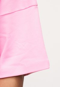 Κοντινό πλάνο σε ροζ ύφασμα μανικιού ή ποδόγυρου με ορατή ραφή σε καφέ δέρμα, αναδεικνύοντας την υφή και την αντίθεση χρωμάτων.