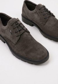 Zapatos de ante gris oscuro con cordones y suelas de goma negras sobre un fondo claro y liso.