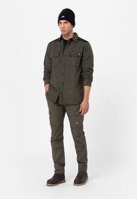 Green flannel shirt with two chest pockets, paired with olive cargo pants and black boots. Black knit beanie completes the outfit.