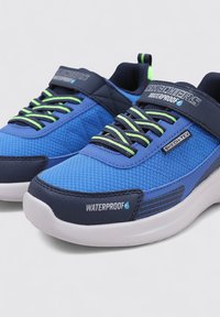Sneaker impermeabili blu con upper in rete e materiale sintetico, lacci verdi a contrasto, colletto imbottito e suola in gomma bianca con dettagli testurizzati.