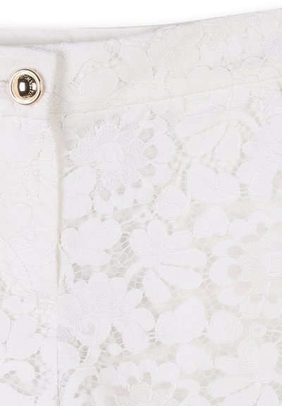 Tissu en dentelle blanche présentant des motifs floraux avec une finition texturée. Comprend un détail de bouton doré à la taille.