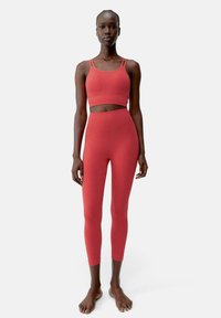Set di reggiseno sportivo e leggings aderenti rossi, realizzati in tessuto elasticizzato, con spalline sottili e design senza cuciture per comfort e flessibilità.