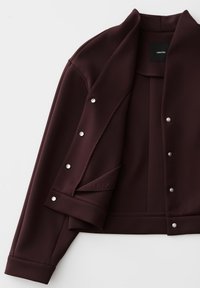 Dark brown jacket with snap buttons on front and cuffs, folded open to show inside and collar, lying flat on a white surface.