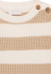 Pull en maille rayé crème et beige avec un col rond côtelé et deux boutons en bois à l'épaule. Tissu texturé avec des rayures alternées.
