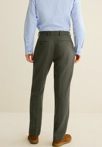 Pantalons à carreaux gris avec poches arrière, portés avec une chemise à manches longues bleu clair et des chaussures marron, mettant en valeur la texture et le motif du tissu.