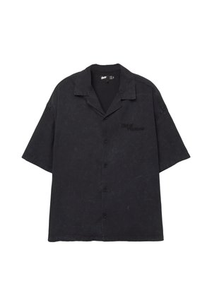 Zwarte kortslibberige button-up shirt van gestructureerde stof. Heeft een kraag en een voorzak met de tekst "Out of The Norm."