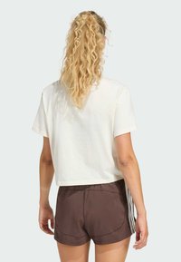 Lichtbeige cropped t-shirt met korte mouwen, gecombineerd met bruine sportshorts met zijstrepen. Gladde stofstructuur.