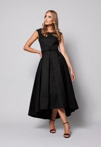 Czarna sukienka z teksturowanym materiałem, dopasowanym gorsetem i sylwetką w kształcie litery A. Posiada rękawy typu cap, detal z guzikami oraz asymetryczny dół.