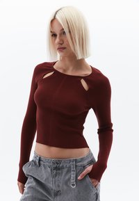 Maglia a maniche lunghe bordeaux a costine con scollatura a girocollo e dettagli con tagli sulle spalle. Abbinata a pantaloni corti grigio chiaro con texture.