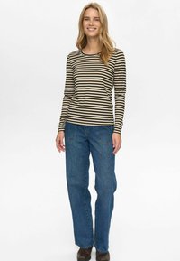 Gestreepte langemouwen top in beige en zwart, gecombineerd met losse blauwe denim jeans. Eenvoudige ronde hals en rechte zoom.