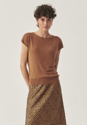 Top scurt de culoare marron, dintr-un material tricotat moale, asortat cu o fustă midi cu imprimeu leopard, având pete negre pe un fond bej.