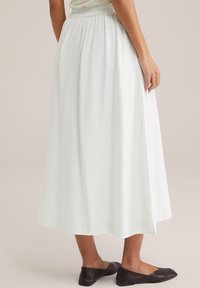 Vit, ankellång kjol med resårmidja, mjuk textur, lättviktsmaterial och en flödande design. Matchad med mörka glidskor.
