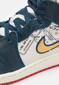 Niebieskie i białe trampki z teksturowanym materiałem, żółtym logo Nike i nadrukowanymi detalami. Posiadają teksturowane sznurowadła i czerwoną podeszwę.