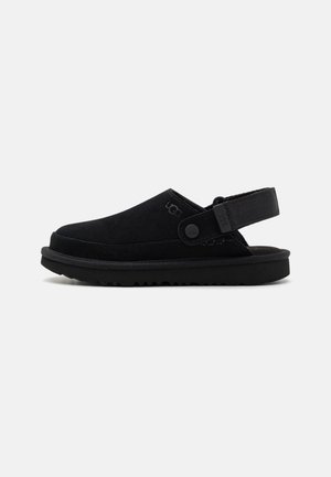 Black suede clog with a flexible heel strap, textured sole, and subtle logo detail on the side, featuring a rounded toe and low profile.