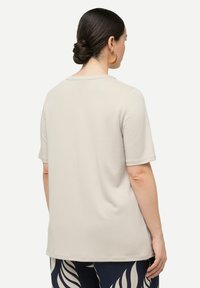 Top corto a maniche corte beige chiaro con taglio dritto e scollatura rotonda. Tessuto liscio, drappeggio sottile e orlo posteriore più lungo.