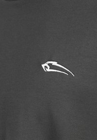 Donkergrijze stof met een gladde textuur, voorzien van een klein wit geborduurd logo aan de linkerkant. Eenvoudig ontwerp met ronde hals.