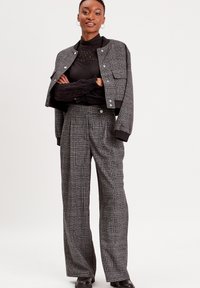 Veste à carreaux grise avec des poignets noirs, assortie à un pantalon à jambes larges à carreaux gris. L'ensemble se distingue par un tissu texturé et des accents en métal argenté.
